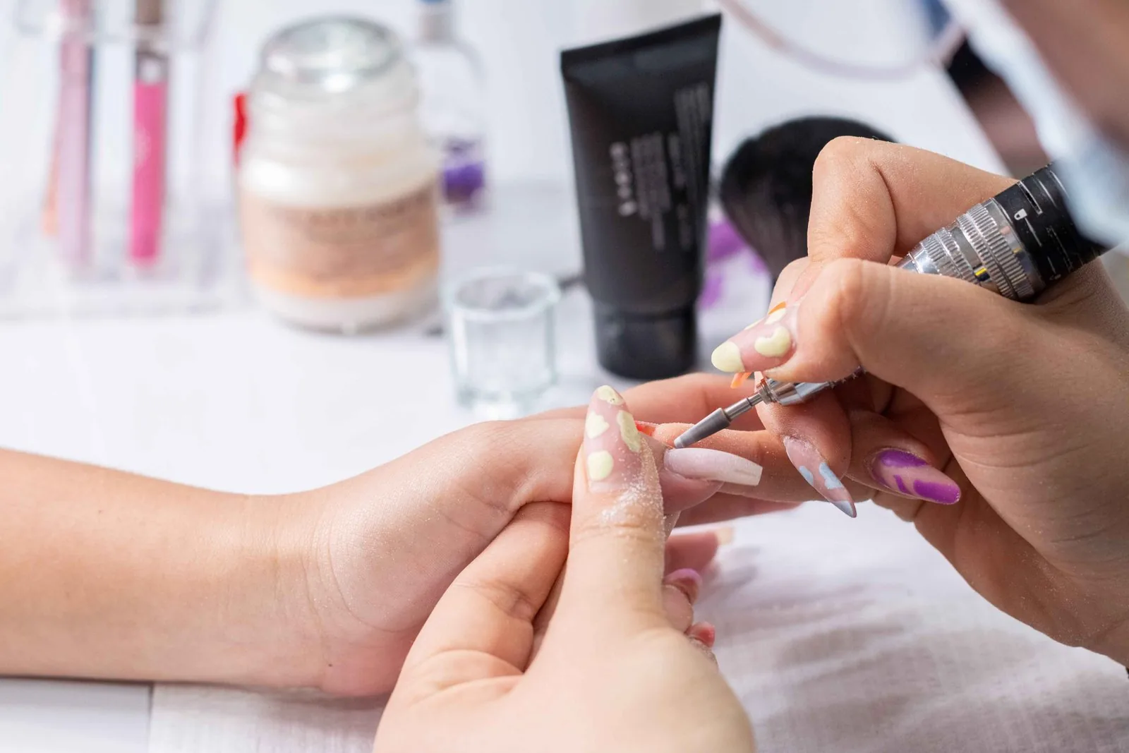 Nail technician filing a woman's white-tipped nails during prep